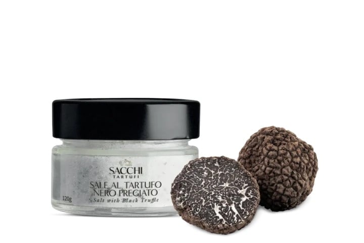 Jar of black truffle salt with two black truffles displayed next to it against a white background